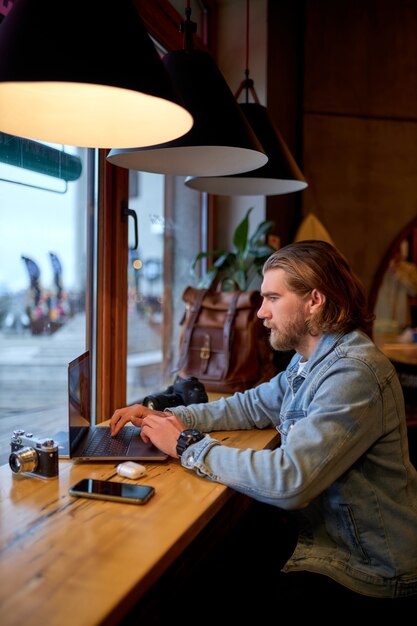 Retrato de um fotógrafo e jornalista barbudo concentrado sentado em um café trabalhando