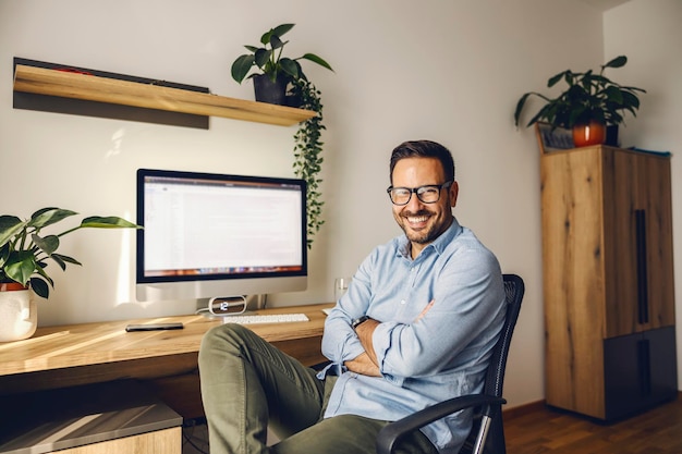 Retrato de um freelancer feliz sentado com os braços cruzados em seu escritório em casa