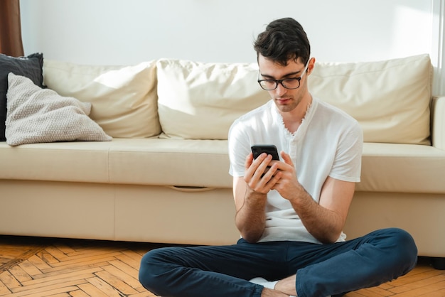 Retrato de um freelancer masculino que está sempre em contato em casa Jovem bonito e focado usando seu smartphone enquanto está sentado no sofá