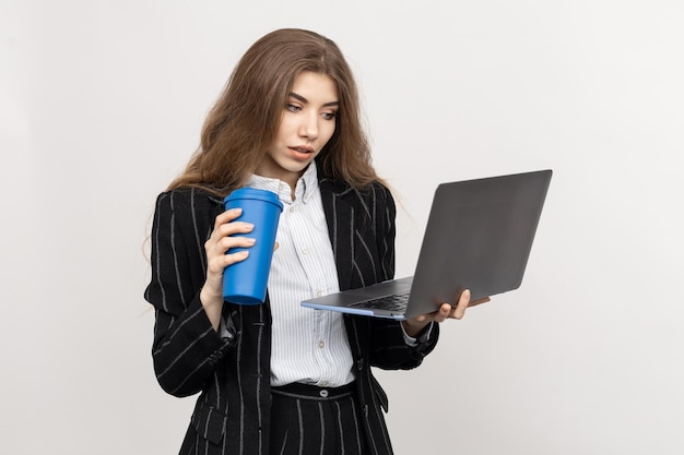 Retrato de um funcionário de escritório que olha atentamente para a tela do laptop e bebe café Uma mulher de terno em um fundo branco