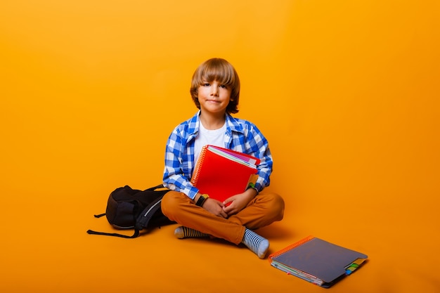 Retrato de um garotinho com um livro sobre um fundo amarelo, estúdio. estudante sentado no chão do estúdio