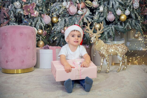 Retrato de um garotinho fofo com um presente nas mãos perto da árvore de natal para o natal