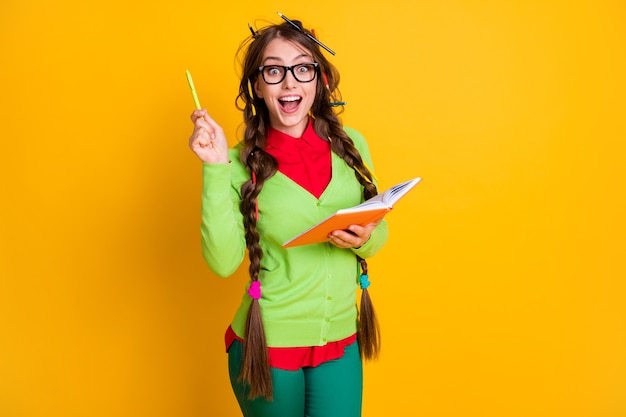 Retrato de um gênio inteligente e animado, uma adolescente alegre, escrevendo uma solução de redação isolada sobre um fundo de cor amarela brilhante