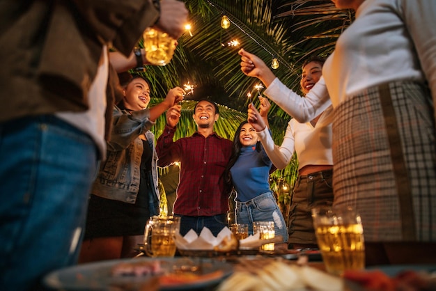 Retrato de um grupo de amigos asiáticos felizes se divertindo com fogos de artifício ao ar livre jovens se divertido com foguetes à noite pessoas comida bebida estilo de vida conceito de celebração de ano novo