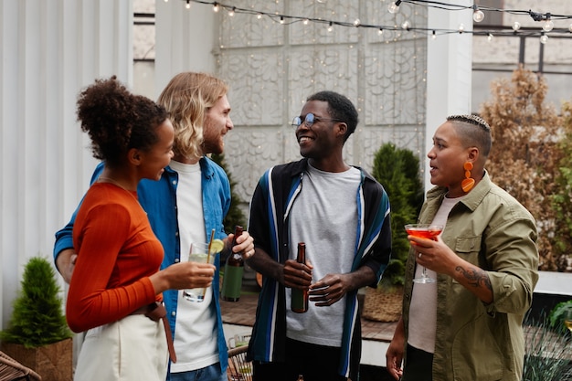 Retrato de um grupo diversificado de jovens se divertindo em uma festa ao ar livre na cobertura e conversando