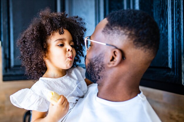 Foto retrato de um homem abraçando uma garotinha em casa e comendo banana