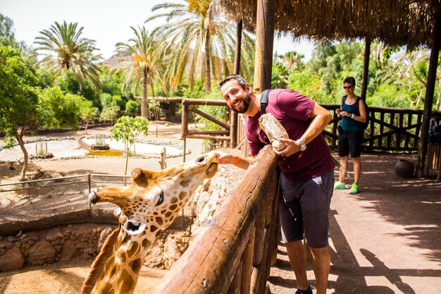 Foto retrato de um homem adulto a alimentar uma girafa no zoológico