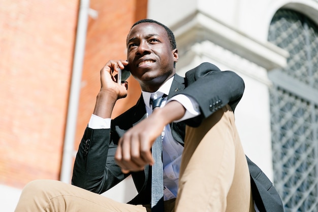 Retrato de um homem africano bonito, sorrindo quando ele está usando seu celular na rua.