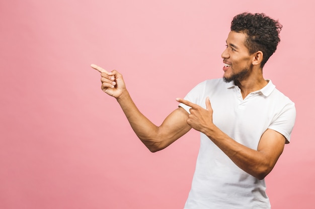 Retrato de um homem africano feliz de sorriso em apontar ocasional com os dedos isolados de lado sobre o fundo cor-de-rosa.