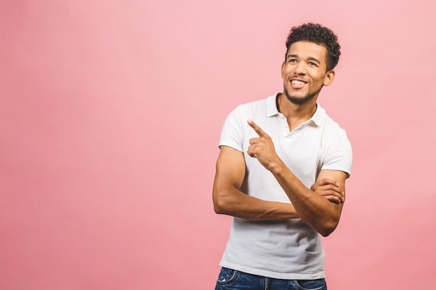 Foto retrato de um homem africano feliz de sorriso em apontar ocasional com os dedos isolados de lado sobre o fundo cor-de-rosa.