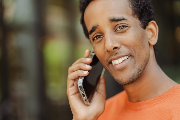 Retrato de um homem afro-americano bonito e sorridente falando no celular atendendo chamada olhando para longe na rua urbana Conceito de tecnologia de negócios bem sucedido