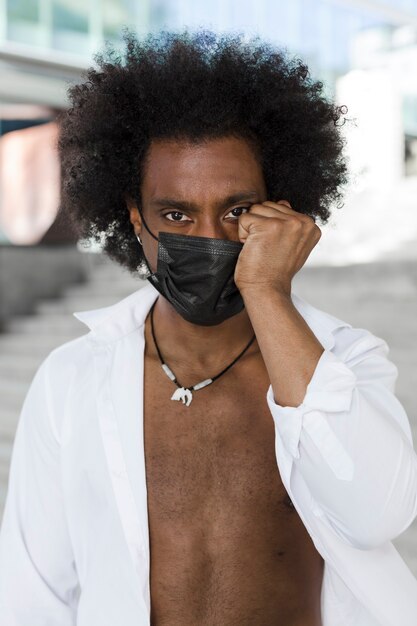 Retrato de um homem afro-americano com máscara facial e uma camisa branca desabotoada.