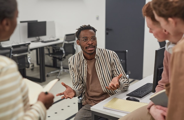 Retrato de um homem afro-americano conversando com colegas de escritório e gesticulando ativamente enquanto colabora no projeto