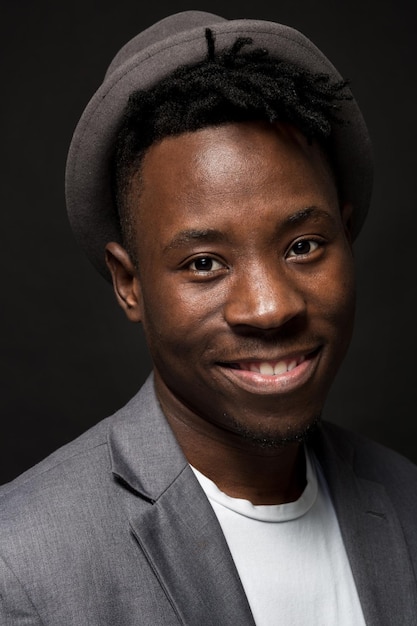 Retrato de um homem afro-americano elegante sorrindo sobre fundo preto. Um cara legal em uma jaqueta cinza e uma camiseta branca em um fundo escuro de estúdio. Um grande retrato