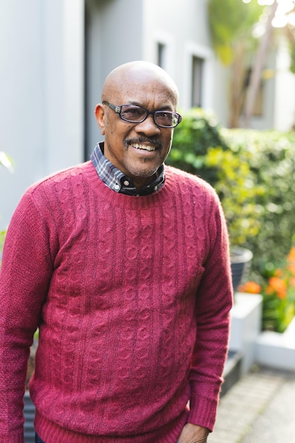 Foto retrato de um homem afro-americano sênior feliz usando óculos e jumper vermelho de pé do lado de fora da casa