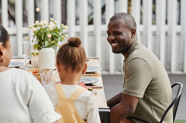 Retrato de um homem afro-americano sorridente, desfrutando de um jantar com a família ao ar livre no terraço cópia espaço