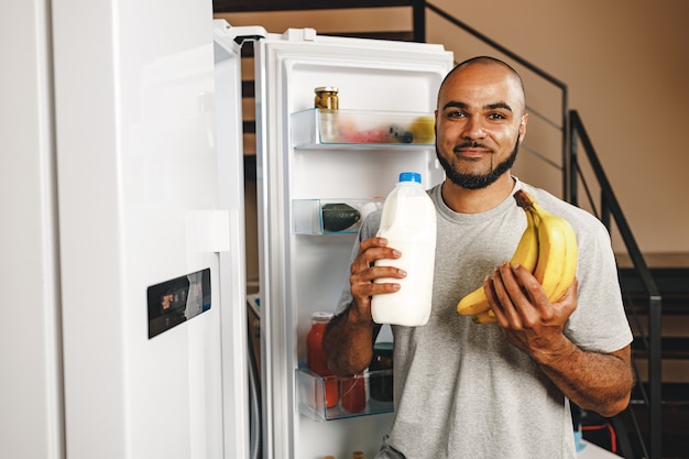 Foto retrato de um homem afro-americano tirando comida de uma geladeira em sua casa