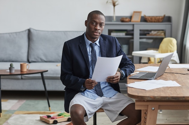 Retrato de um homem afro-americano vestindo jaqueta e shorts enquanto trabalha em casa e olhando para a câmera, copie o espaço