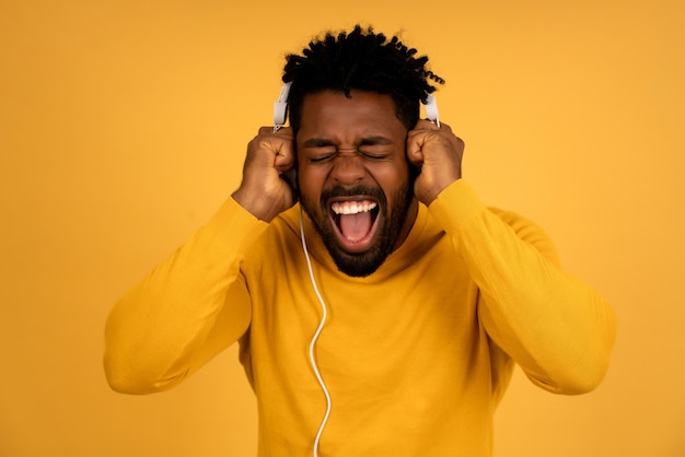 Retrato de um homem afro, curtindo ouvir música com fones de ouvido em pé contra um fundo amarelo isolado.