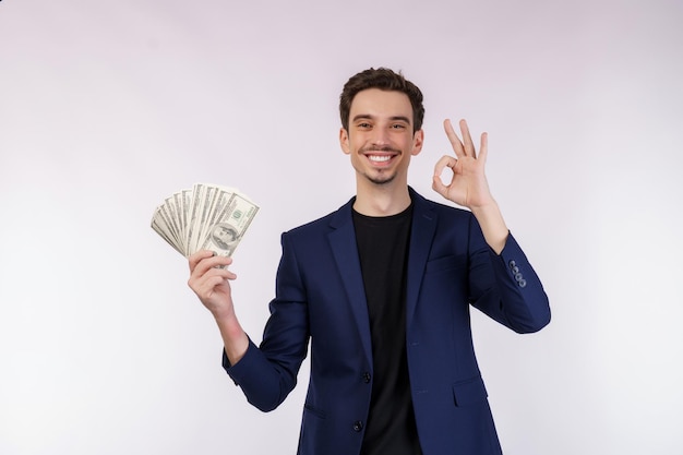 Retrato de um homem alegre mostrando sinal de ok e segurando dinheiro sobre fundo branco