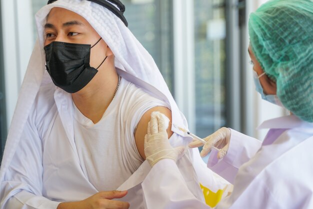 Retrato de um homem árabe muçulmano olhando enquanto toma a vacina covid na clínica ou hospital
