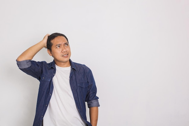 Retrato de um homem asiático casual coçando o cabelo com uma expressão confusa no fundo branco