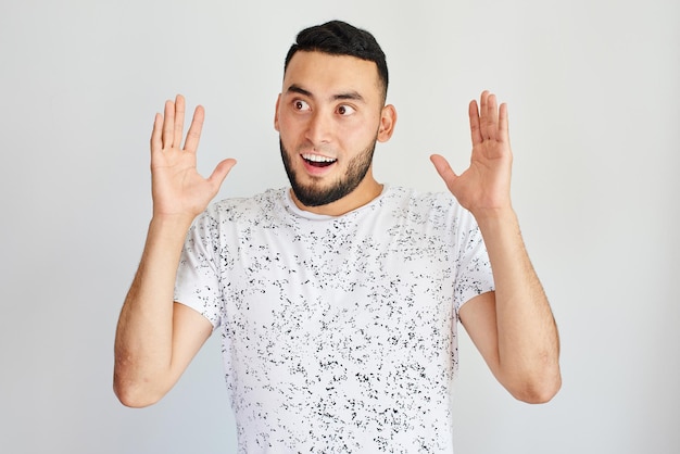 Retrato de um homem asiático do Cazaquistão animado com a boca aberta de surpresa levantando as mãos em um fundo branco de estúdio