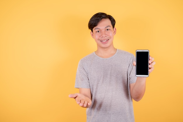 Retrato de um homem asiático sorridente mostrando o celular de tela em branco enquanto está em fundo amarelo