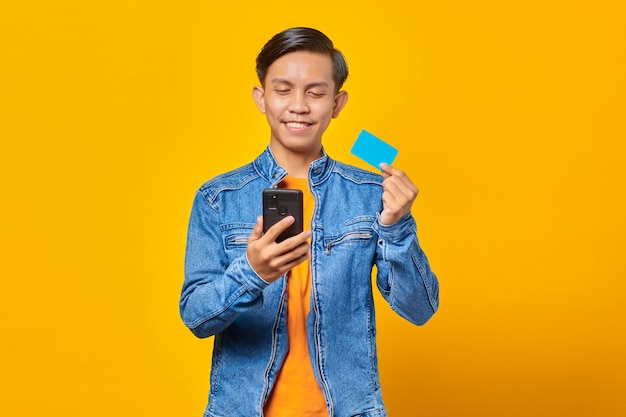 Retrato de um homem asiático sorridente usando cartão de crédito para pagar com celular