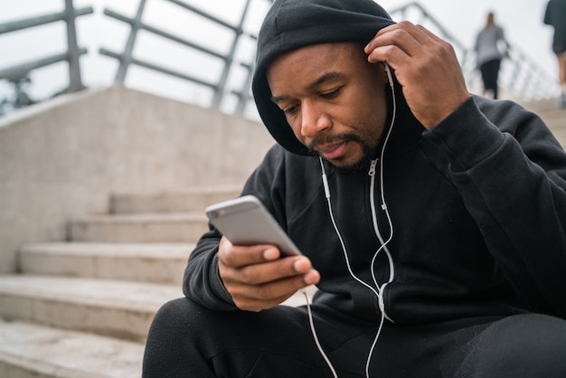 Retrato de um homem atlético usando seu telefone celular durante uma pausa do treino enquanto está sentado na escada de concreto. Conceito de esporte e saúde.