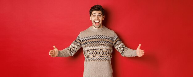 Retrato de um homem atraente feliz com suéter de Natal, mostrando o grande presente espalhar as mãos para os lados enquanto eu ...