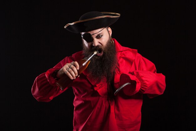 Retrato de um homem barbudo atraente vestido como um pirata para o halloween. Pirata tentando abrir a garrafa com a boca.