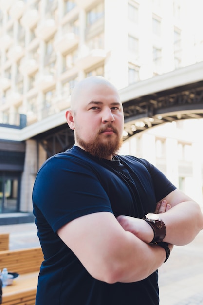 Foto retrato de um homem barbudo bonito careca em uma camiseta preta na rua, que parece longe.