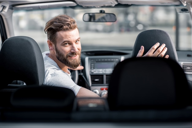 Retrato de um homem barbudo bonito olhando para trás, sentado no banco da frente do carro