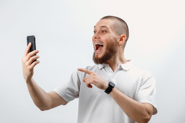 Retrato de um homem barbudo bonito positivo em uma camiseta branca falando na chamada de vídeo usando um smartphone