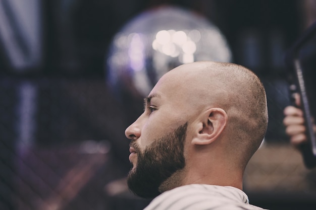 Retrato de um homem barbudo bonito sentado em uma cadeira em uma barbearia