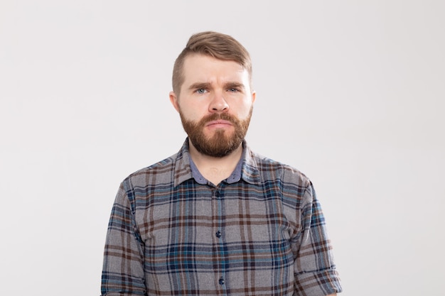 Retrato de um homem barbudo duvidoso, vestindo uma camisa xadrez casual, olhando com expressão indecisa no rosto, mostrando dúvida e hesitação