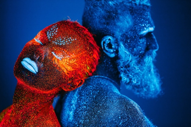 Foto retrato de um homem barbudo e uma mulher pintados em pó ultravioleta.