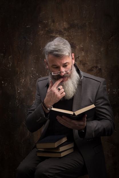 Foto retrato de um homem barbudo grisalho com óculos, lendo o livro