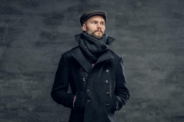 Retrato de um homem barbudo hipster vestido com uma jaqueta cinza e um gorro de lã isolado em fundo cinza.