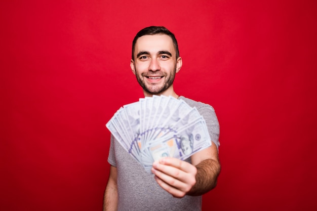 Retrato de um homem barbudo satisfeito com uma camiseta preta demonstrando a nota de dinheiro em moeda de 100 dólares na câmera isolada sobre a parede vermelha