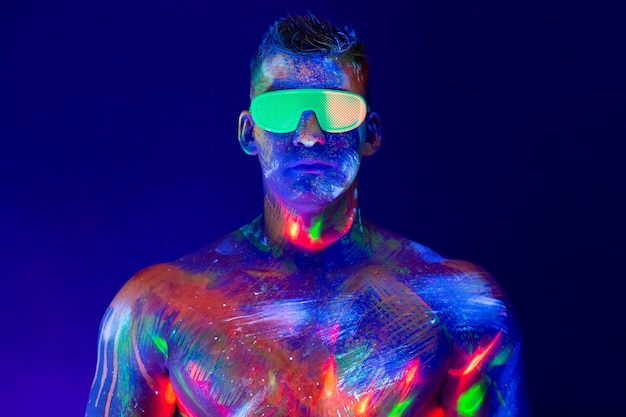 Retrato de um homem bombeado em uma discoteca. Tinta fluorescente no rosto com luz UV