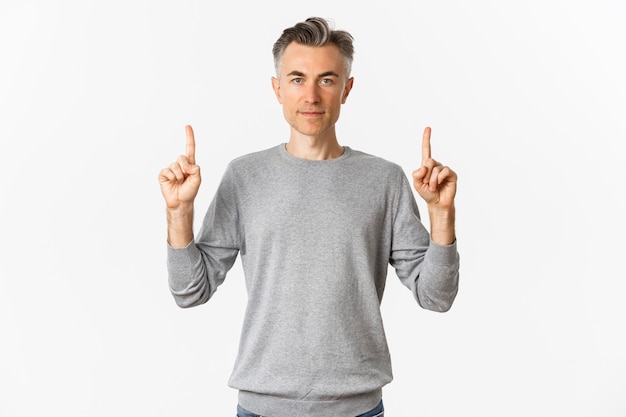Retrato de um homem bonito de meia-idade com suéter cinza, mostrando uma promoção e apontando o dedo para cima