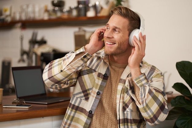 Retrato de um homem bonito e feliz, freelancer, trabalhando e ouvindo música em fones de ouvido sem fio