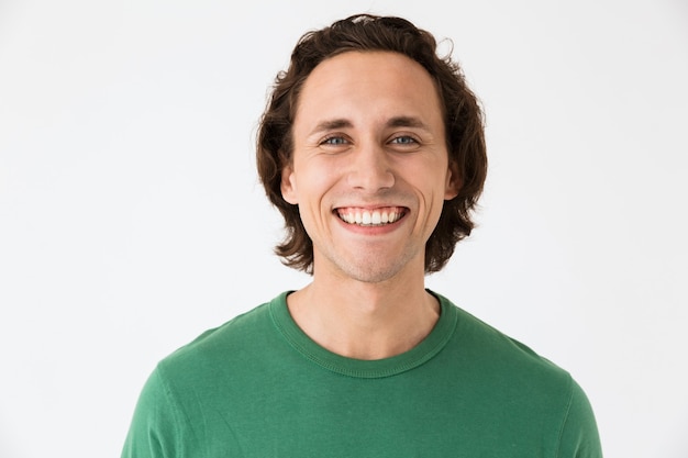 Retrato de um homem bonito e moreno vestindo uma camiseta básica, sorrindo para a câmera, isolada na parede branca