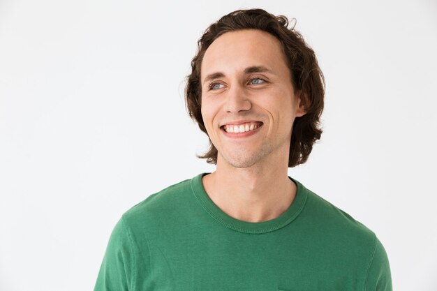 Retrato de um homem bonito e moreno vestindo uma camiseta básica, sorrindo para a câmera, isolada na parede branca