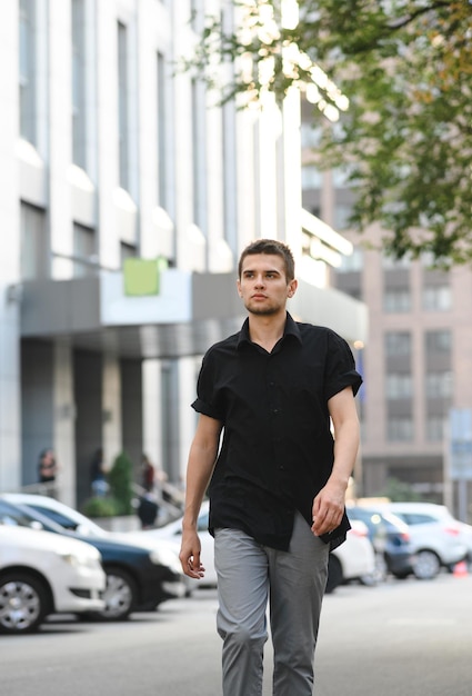 Retrato de um homem bonito em roupas casuais andando na rua em um fundo da paisagem urbana