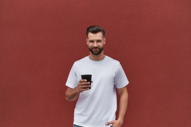 Retrato de um homem bonito em roupas casuais segurando uma xícara de café e olhando