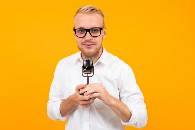 Retrato de um homem bonito em uma camisa branca com um microfone retrô cantando em uma parede amarela