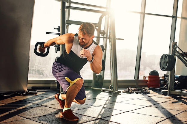 Retrato de um homem bonito fazendo exercícios de flexões com equipamentos modernos de peso no ginásio de fitness